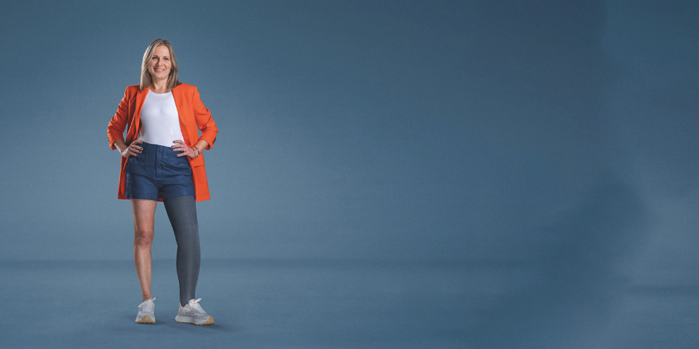 A woman standing up wearing compression garments and an orange jacket A woman standing up wearing compression garments and an orange jacket